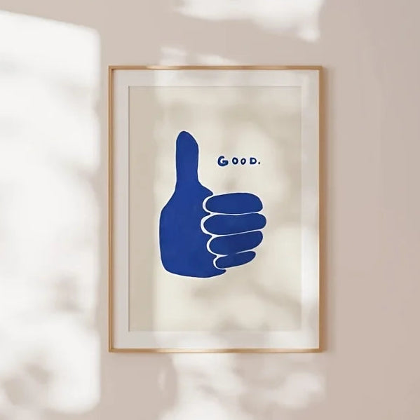 Framed artwork of a blue hand giving a thumbs up with 'Good' text on a beige wall.