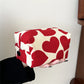 Red and white heart-patterned pouch held by a person against a neutral background
