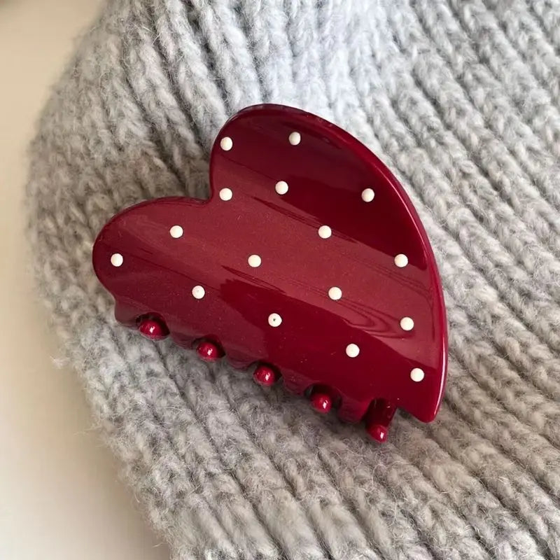Red heart-shaped hair clip with white polka dots on a gray textured background