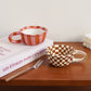 Two checkered ceramic bowls on a wooden surface with a book and fork.