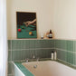 Bathroom with green and white striped tiles, bathtub, and decorative painting.