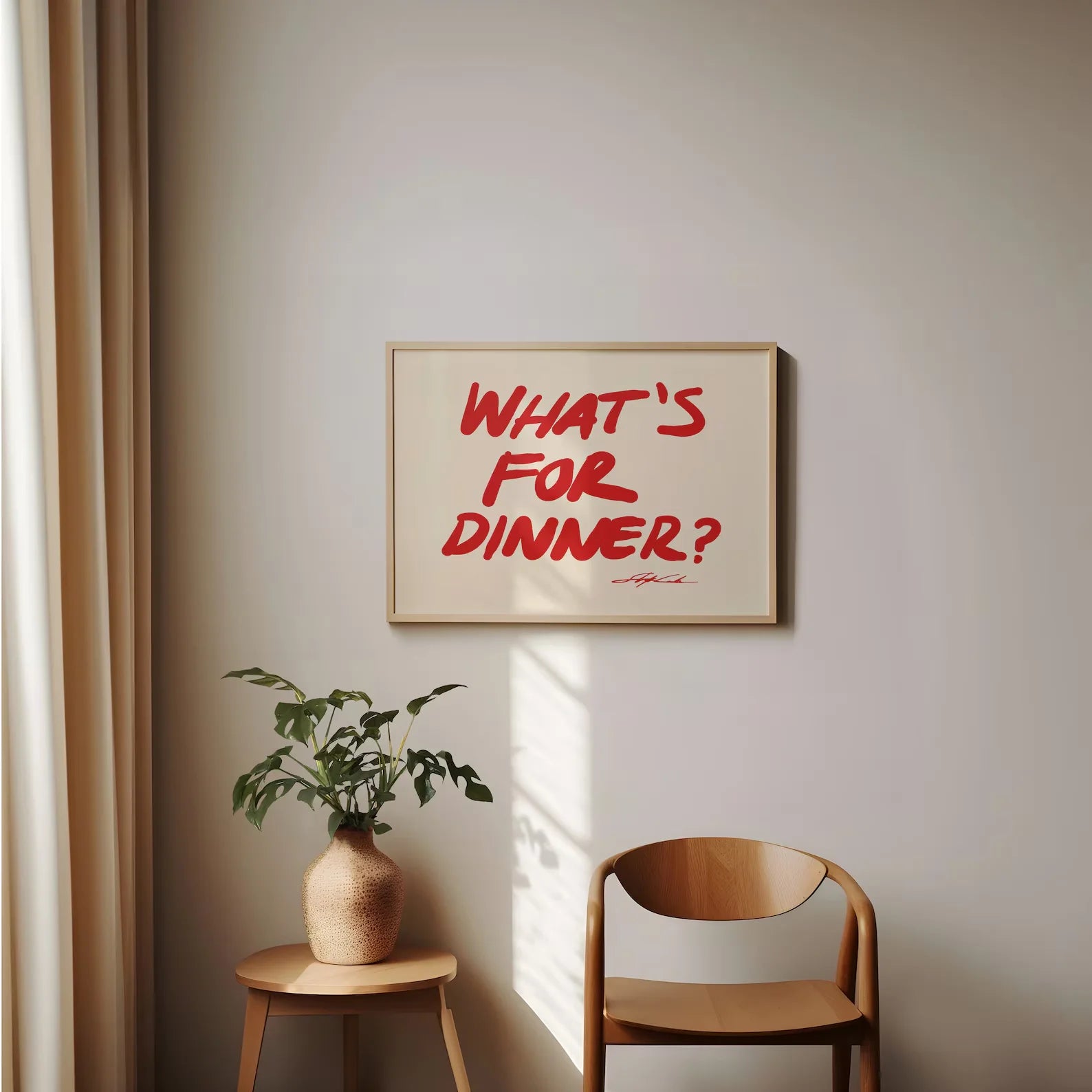 Framed artwork with 'What's for Dinner?' text on a wall above a wooden chair and plant.