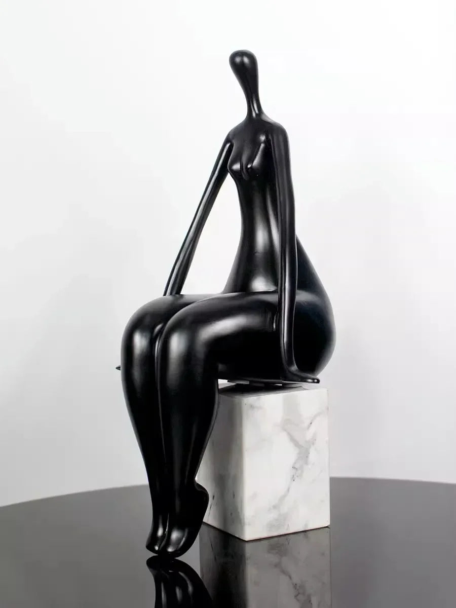 Black abstract sculpture on a marble base against a white background