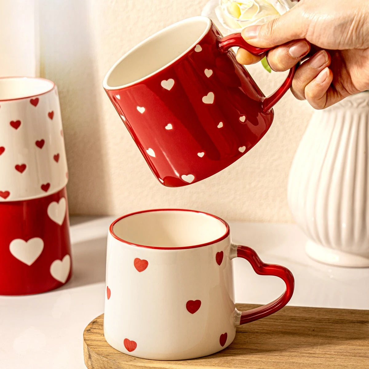 Red and white mugs with heart patterns on a wooden surface.
