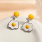Fried egg-shaped earrings with yellow yolks on a beige background