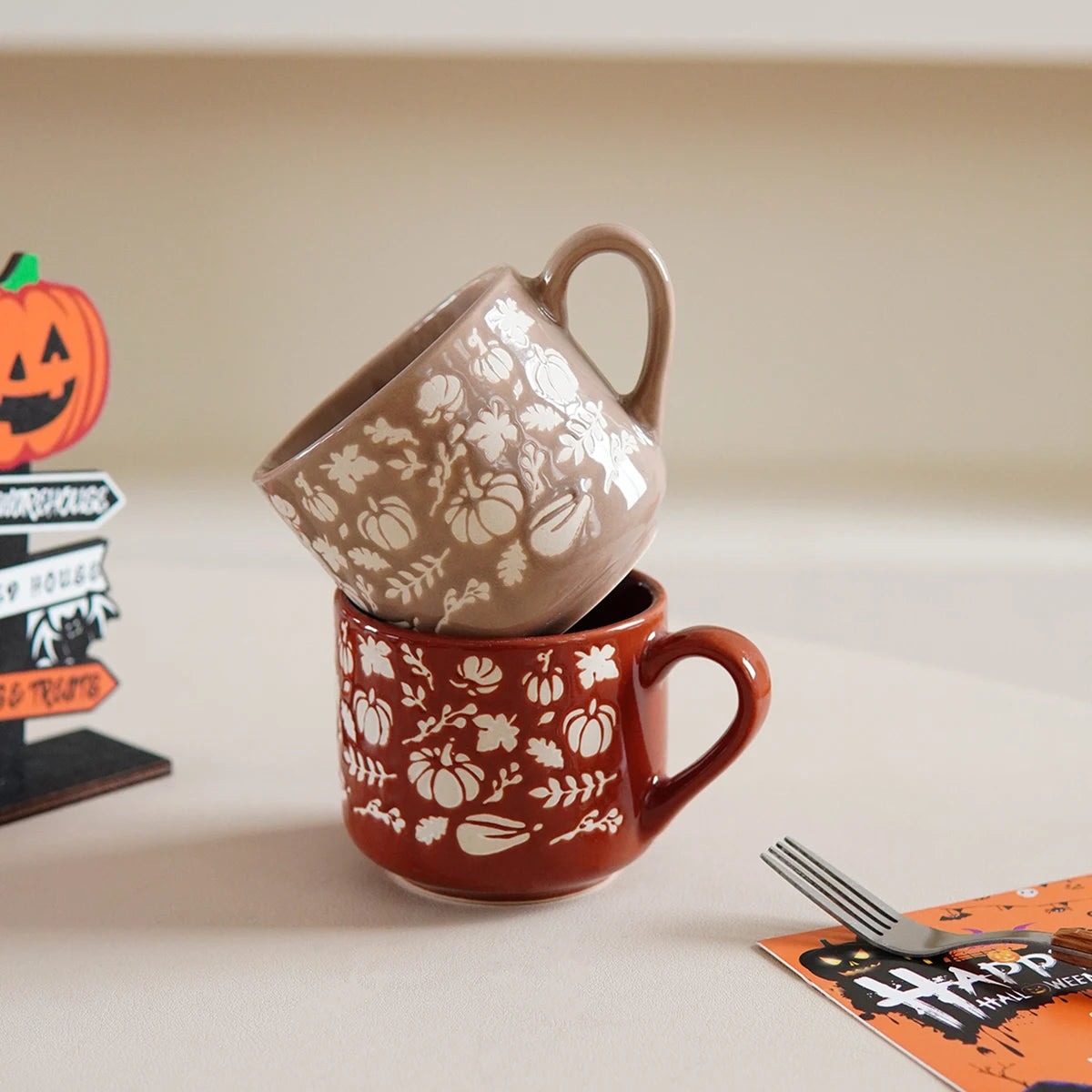 Two ceramic mugs with Halloween-themed designs stacked on a neutral background