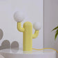 Yellow cactus-shaped lamp with two white spherical lights on a white surface.