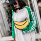 Person wearing a green and white sweatshirt with a banana design, standing in front of a glass door.
