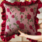 Decorative pillow with floral pattern and red ruffle held by a hand against a neutral background