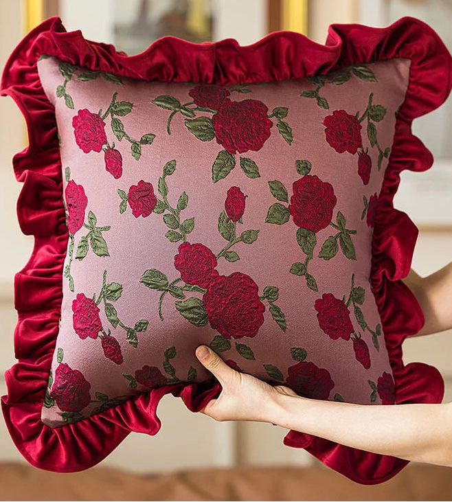 Decorative pillow with floral pattern and red ruffle held by a hand against a neutral background