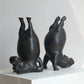 Two black ceramic sculptures of dogs standing on their hind legs on a white surface with a light gray background.