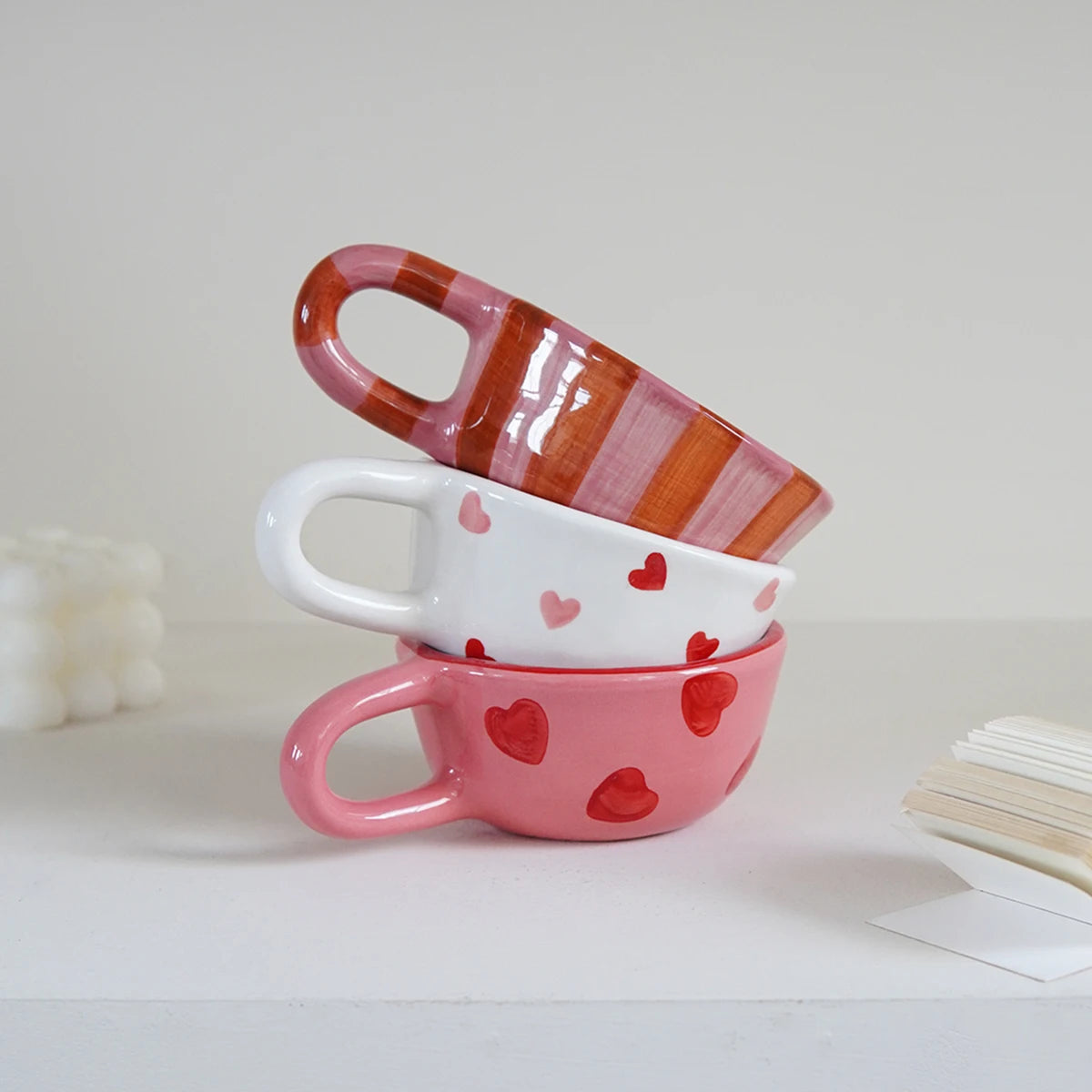 Stack of ceramic mugs with red heart patterns on a white background