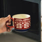 Hand holding a red and white mug with floral design in front of an open microwave.