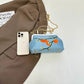 Blue handbag with floral design next to a smartphone on a brown fabric background