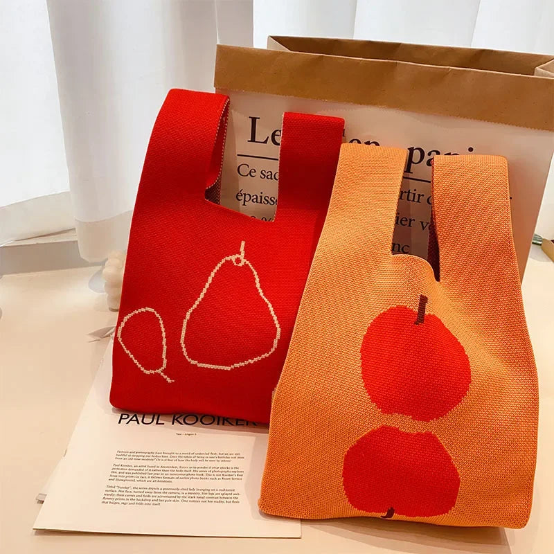 Two knitted bags, one red with a pear design and one orange with an apple design, on a surface.