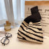 Black and white striped bag on a surface with glasses, perfume bottle, and paper in the background.