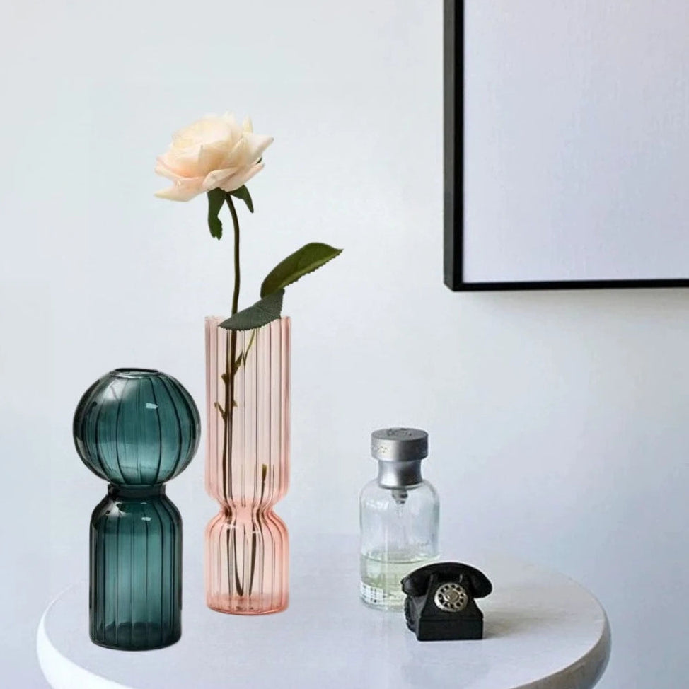 Three glass vases on a white surface with a framed picture in the background.