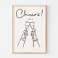 Framed artwork with 'Cheers!' text and line drawings of clinking champagne glasses on a white background.