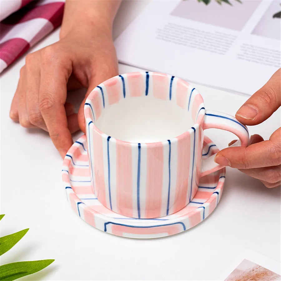 Person holding a striped ceramic cup and saucer with a white background