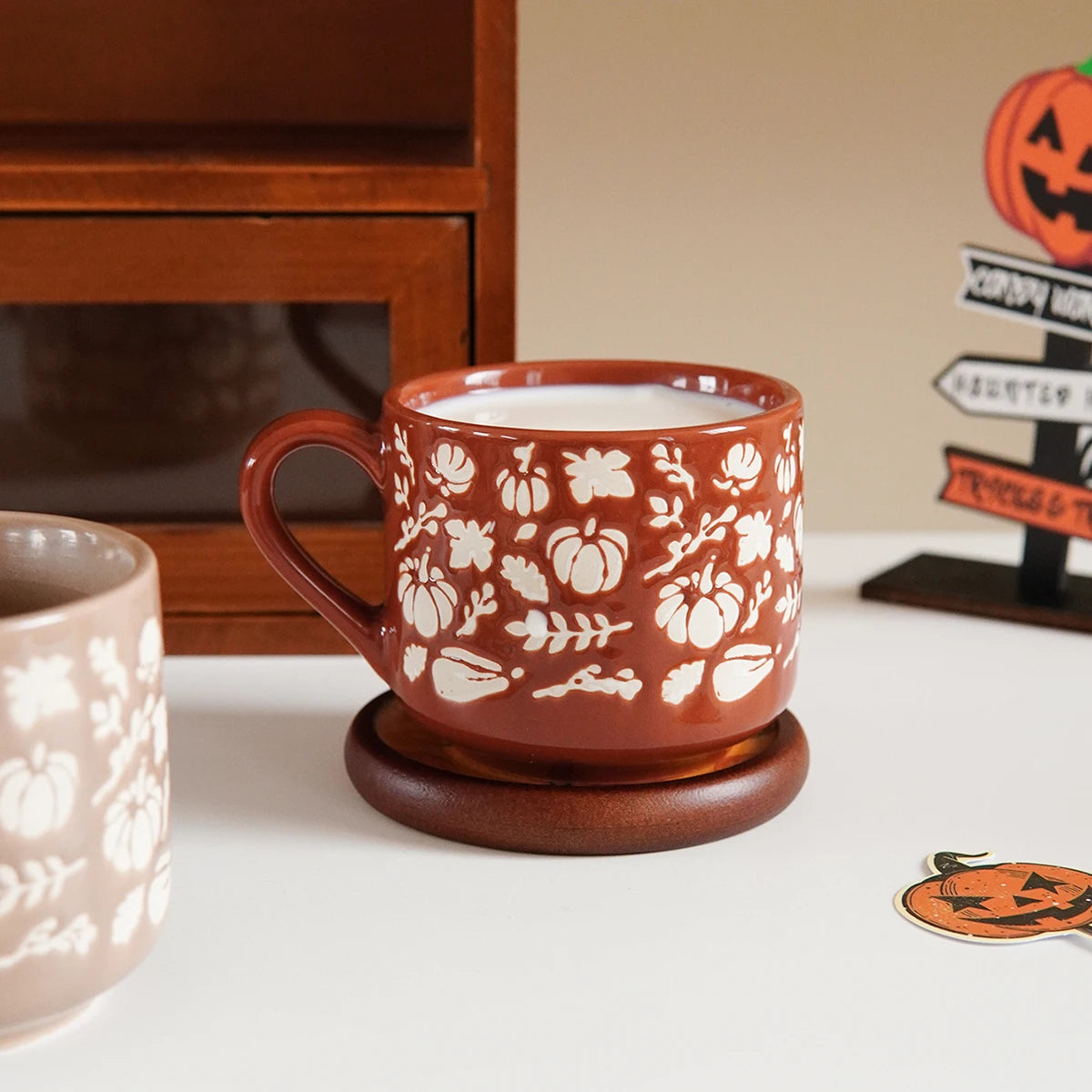 Ceramic mug with floral and pumpkin design on a white surface with Halloween decorations.