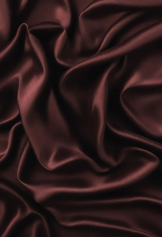 Rich burgundy satin fabric draped elegantly on a surface, showcasing deep folds and a luxurious sheen in soft lighting