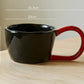 Black mug with red handle on a wooden surface, showing measurements and weight capacity.