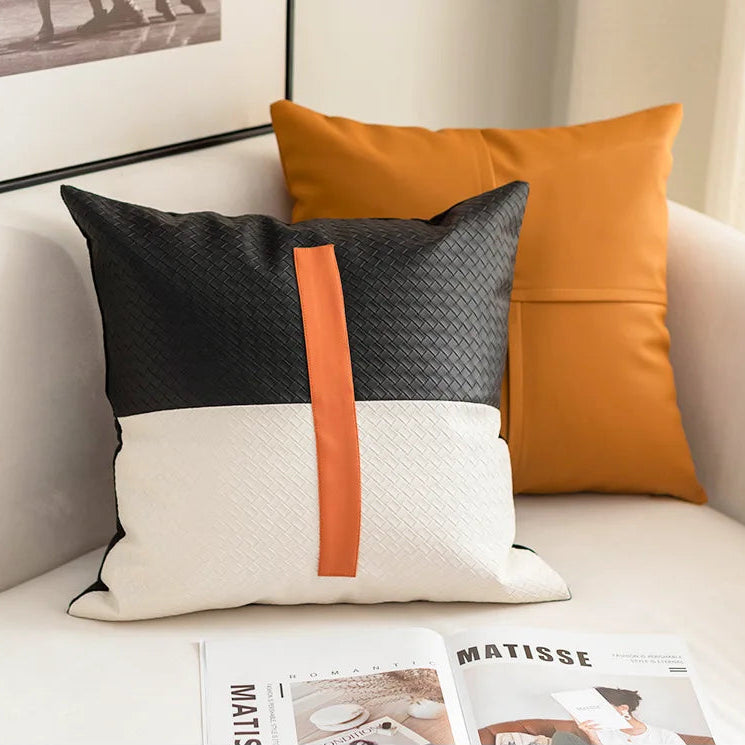 Decorative pillows with black, white, and orange design on a sofa with a magazine underneath.