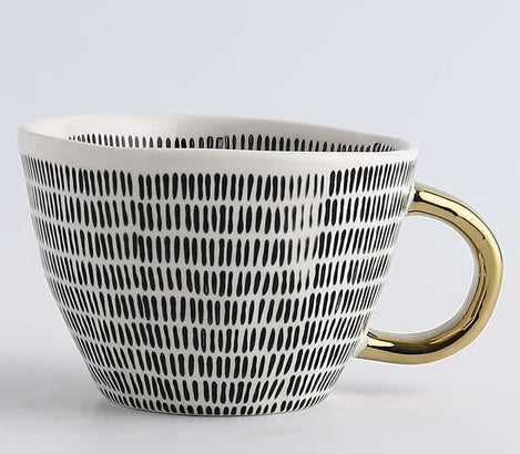 Ceramic mug with black pattern and gold handle on a light gray background, featuring the brand 'Fantasy'.