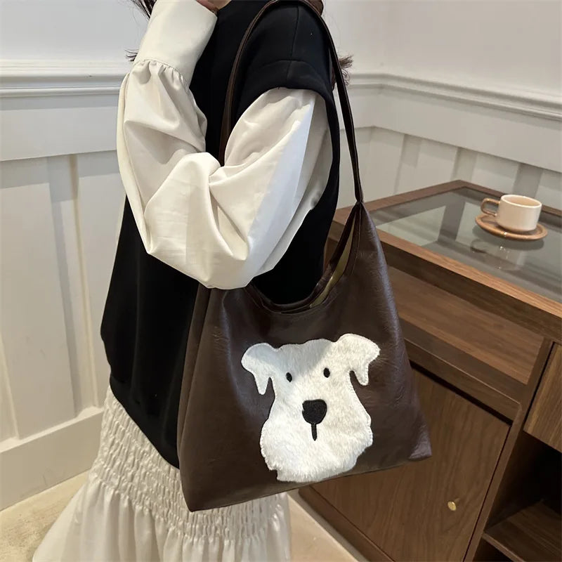 Person holding a brown tote bag with a dog face design in a room.