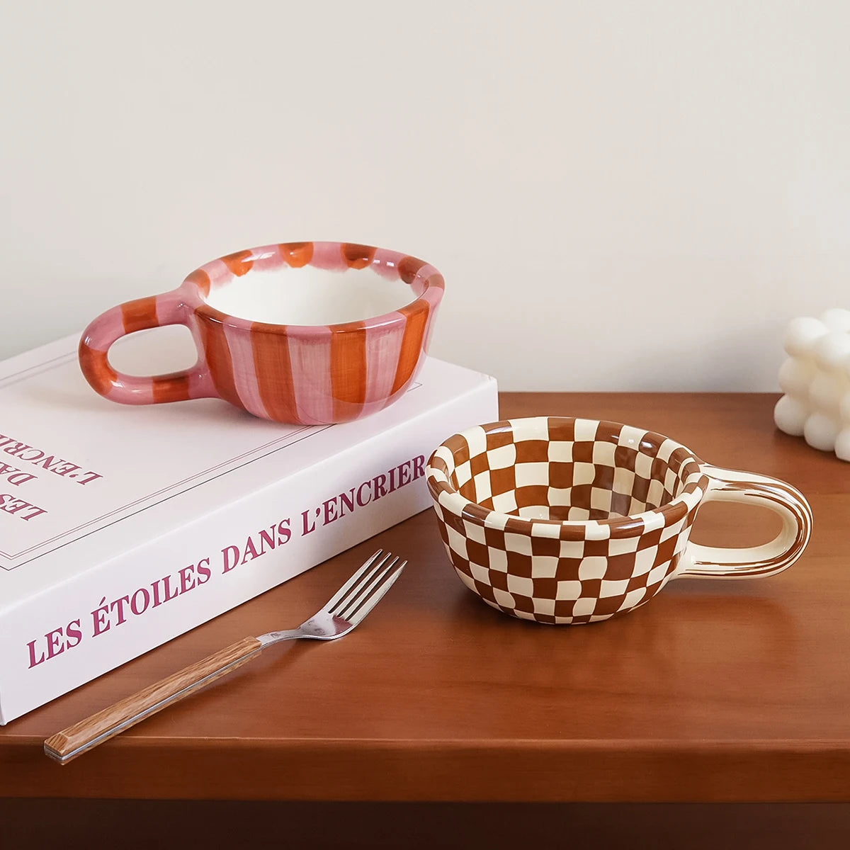 Two checkered ceramic bowls on a wooden surface with a book and fork.