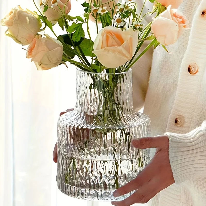Clear textured vase with flowers held by a person wearing a white sweater.