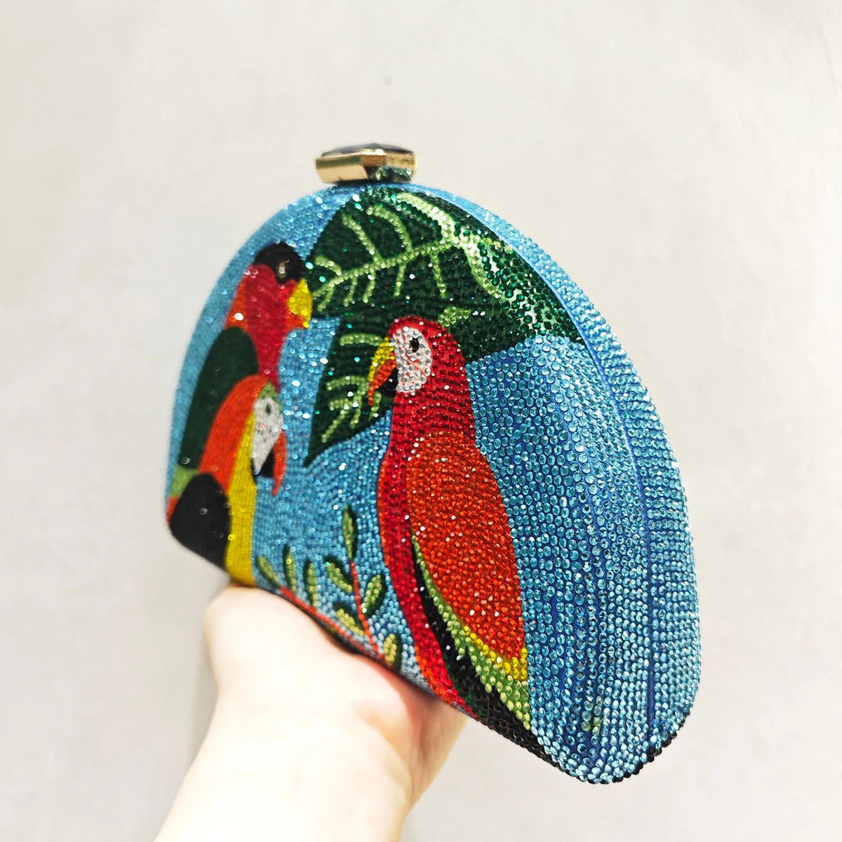 Colorful beaded clutch with parrot design held by a hand against a plain background