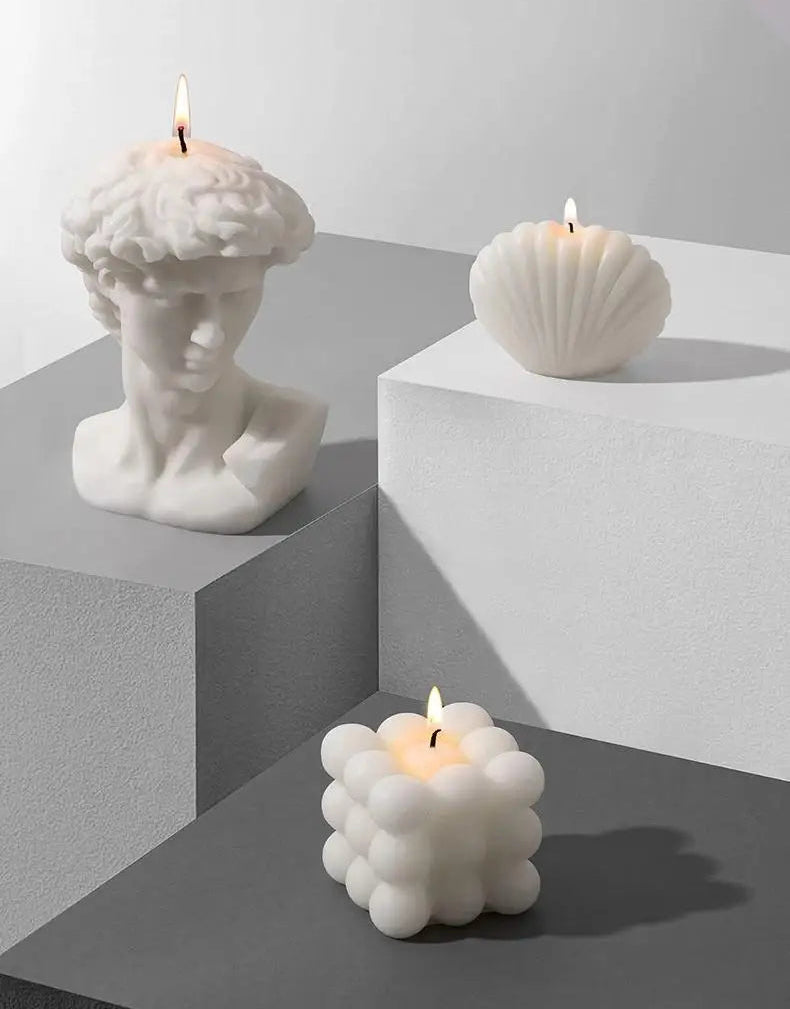 Three white candles, including a bust, shell, and bubble design, on a geometric gray surface - alternate view 4