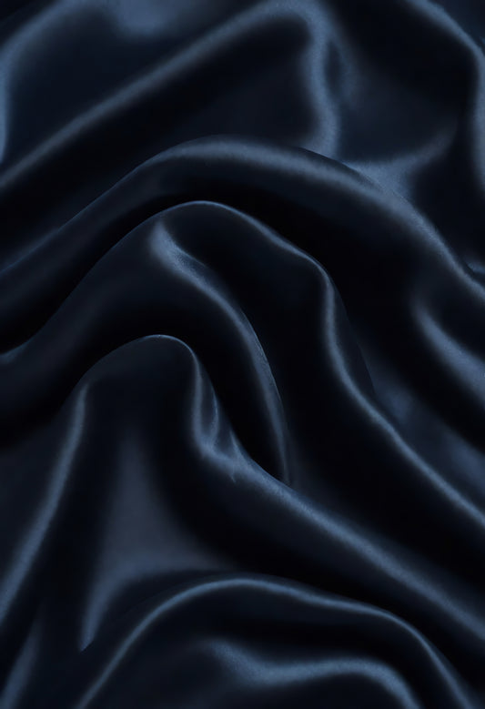 Rich navy blue fabric draped elegantly on a surface, showcasing smooth texture and gentle folds in warm lighting