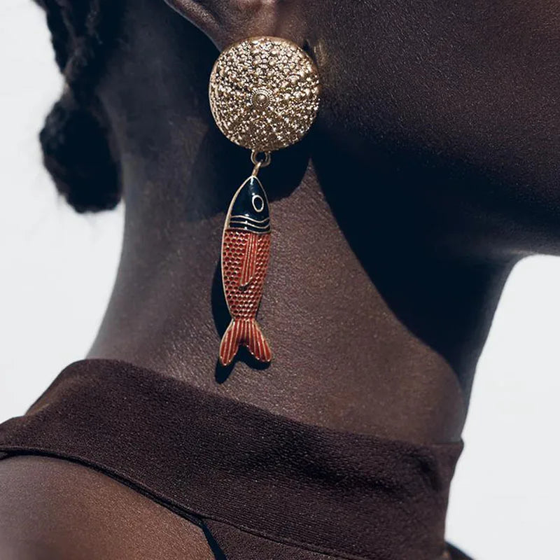 Earring with fish design worn by a person against a neutral background