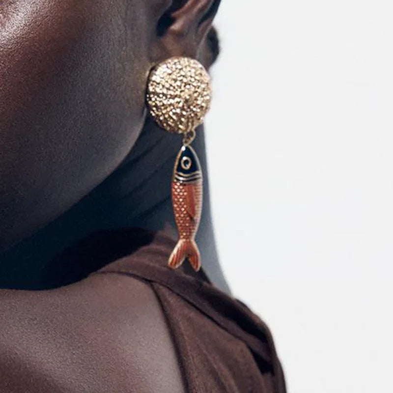 Close-up of a person wearing a fish-shaped earring with a gold top