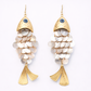 Gold and white fish-shaped earrings on a light gray background