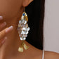 Gold fish-shaped earring with shell details worn by a person