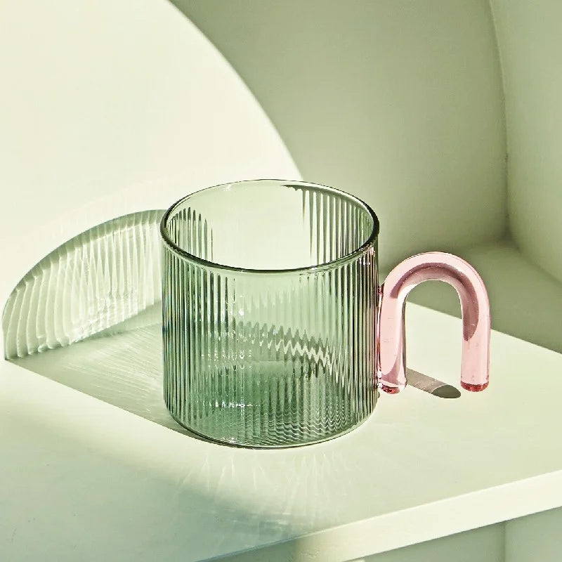 Green glass mug with a pink handle on a white surface