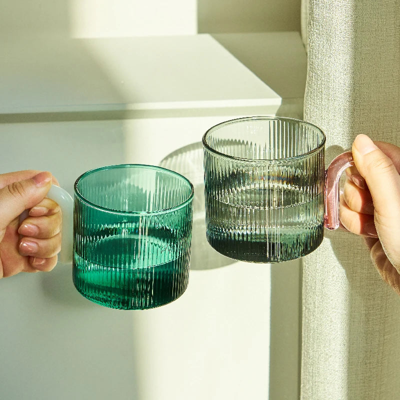 Two hands holding green glass mugs against a neutral background
