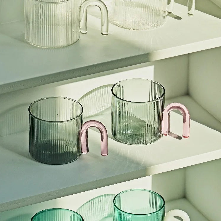 Green glass tumblers with pink handles on a white shelf