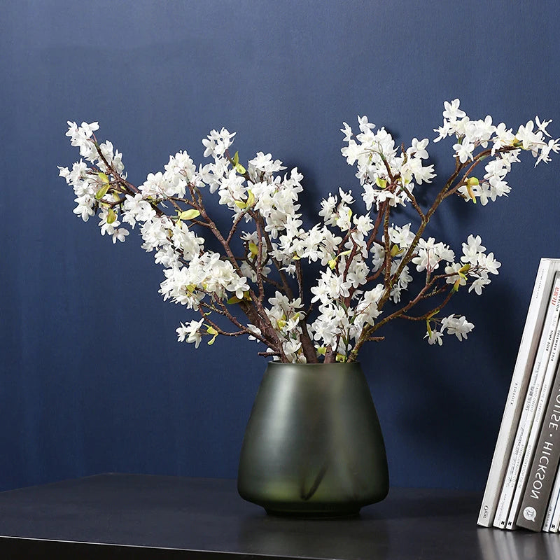 Green glass flower vase styled against a blue wall