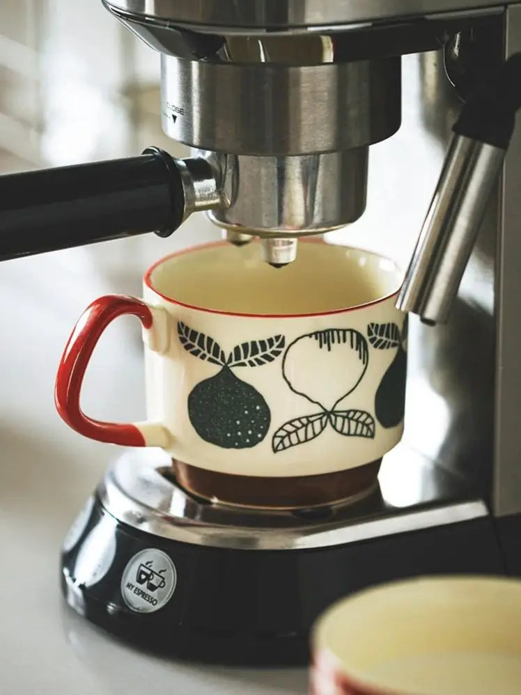 Espresso machine brewing coffee into a decorative mug with fruit design.