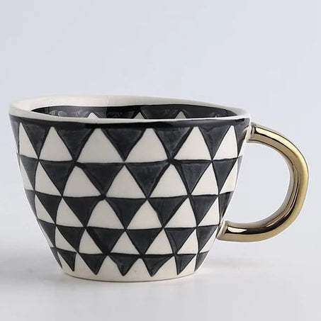Ceramic mug with black and white triangle pattern and gold handle on a light gray background