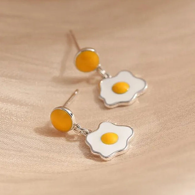 Fried egg-shaped earrings on a beige fabric background