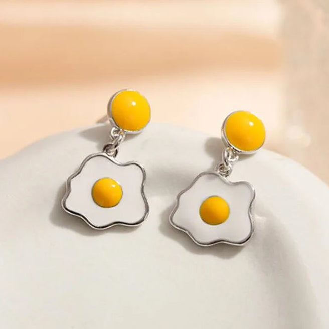 Fried egg-shaped earrings with yellow yolks on a beige background