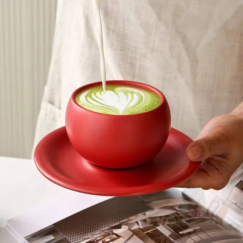 Red cup of green tea with latte art on a red saucer, held by a person.