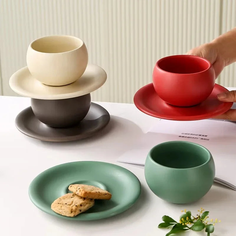 Set of ceramic cups and saucers in various colors on a white surface with a blurred background.