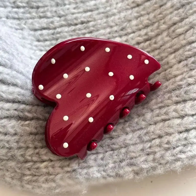 Red hair clip with white polka dots on a textured gray surface