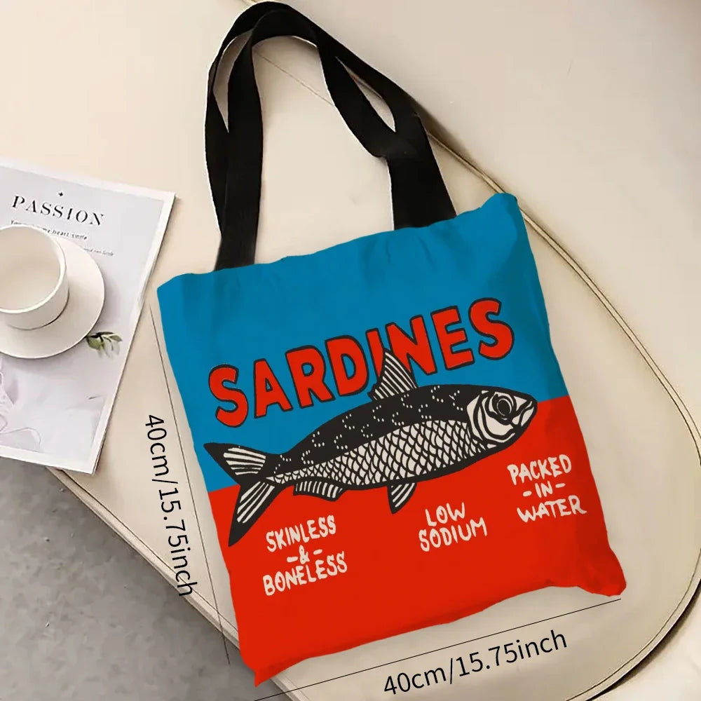 Tote bag with 'Sardines' design on a surface with a magazine and cup.